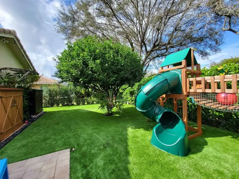 a backyard playground set up with two slides, swings and more, all safely set on artificial grass for playgrounds. Installed by Scottsdale Turf Pros