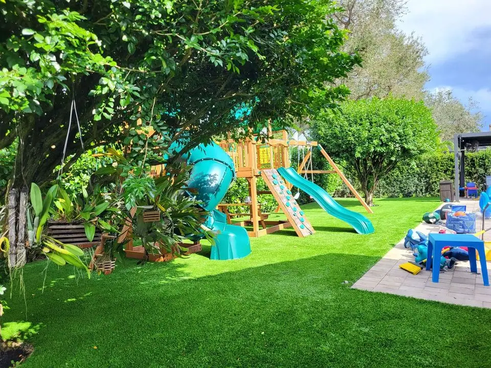 lush green artificial grass with a tree and platground with a slide and a swing bridge. Set in a backyard in scottsdale az