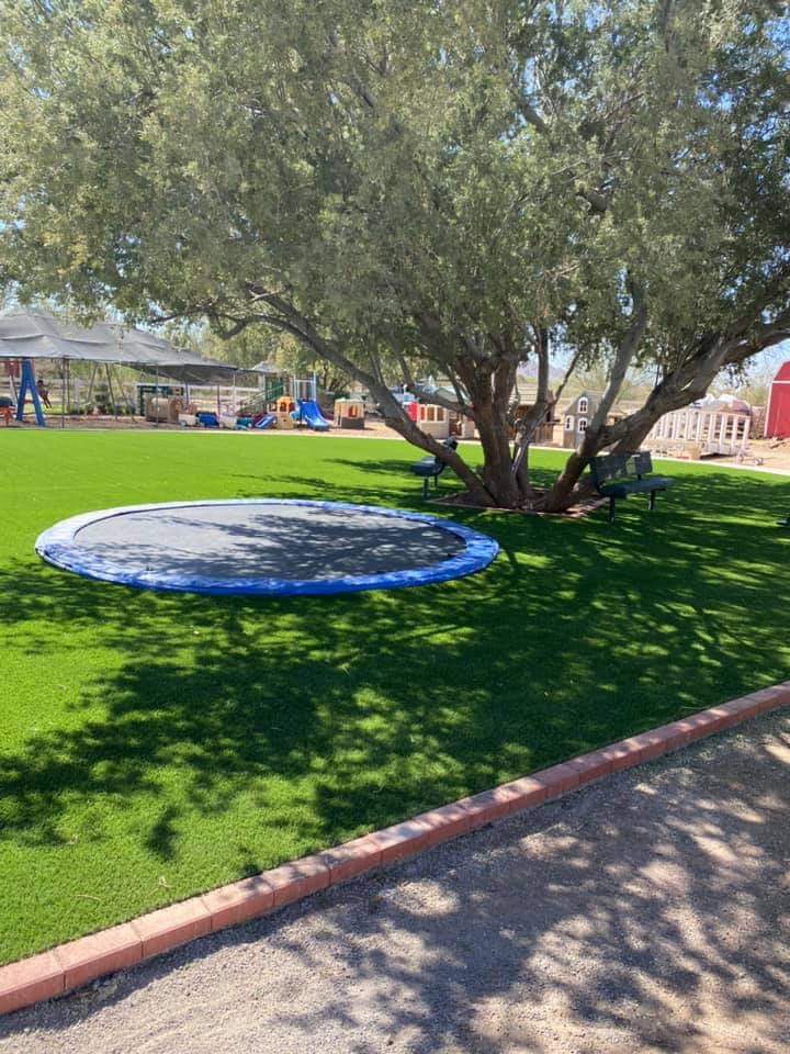 a school in scottsdale AZ with a trampoline set into the ground with artificial turf installed all around it. playground with slides and swings in the background